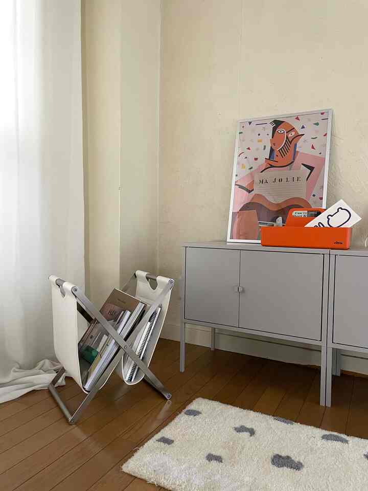 ナチュラルトーンの1LDKリビング、グレーのキャビネットと白いマガジンラック、壁にポスターが配置されたシンプルなインテリア