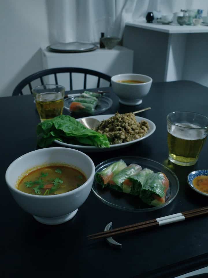 黒いテーブルに透明な皿と白い碗、緑の野菜が置かれたエスニック風の雰囲気あるダイニング