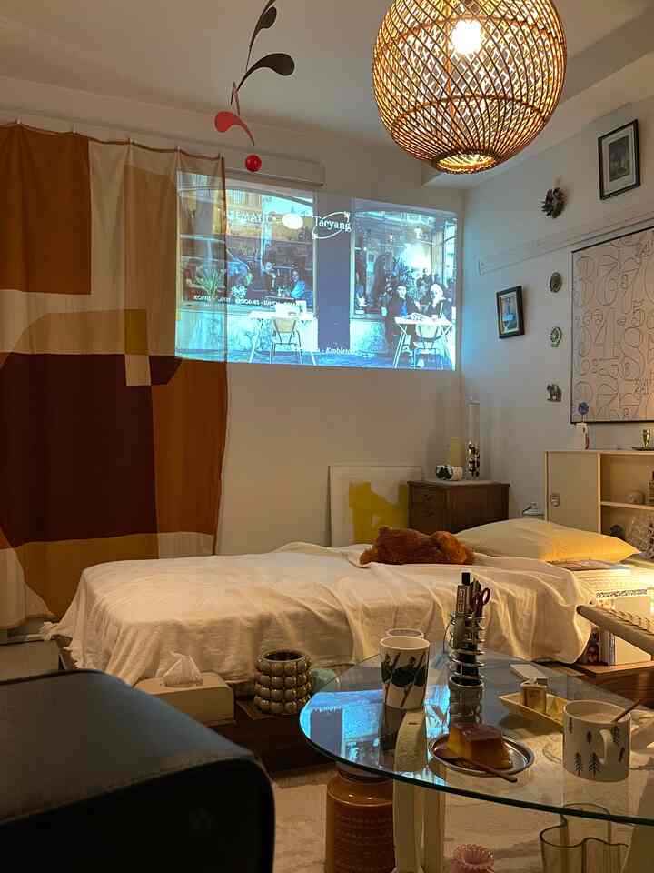 暖かいブラウンとホワイトの色調の一人暮らしリビング、プロジェクタースクリーンと低いベッドが配置された自然な雰囲気のインテリア