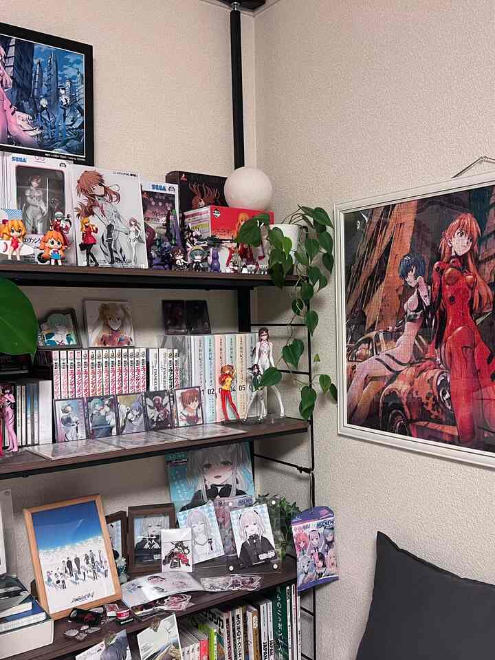 ベージュ色の壁と本棚にアニメフィギュアとポスターが配された趣味の空間