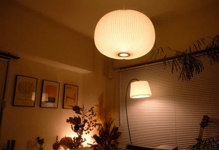 暖かいブラウン調のワンルーム、中央のペンダントライトとフロアランプが柔らかな間接照明を演出する雰囲気のあるインテリア