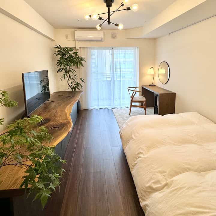 白い壁と寝具、木目調の床と家具が配置された1Kの狭いジャパンディスタイルの寝室空間
