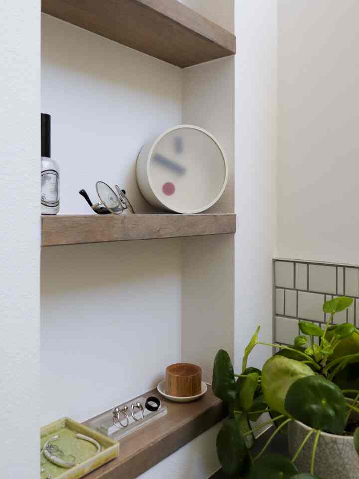 白と茶色の壁棚に小物と時計が配置されたナチュラルでミニマルな空間