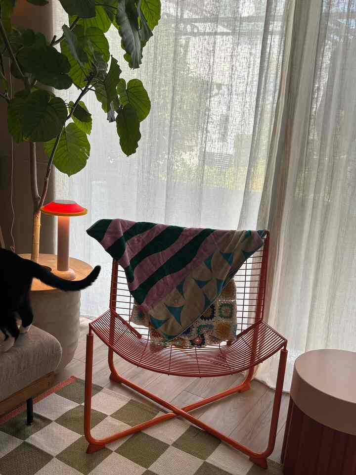 ベージュのトーンが特徴のリビング、オレンジ色のメタルアームチェアにカラフルなタオルが掛けられた雰囲気のあるインテリア