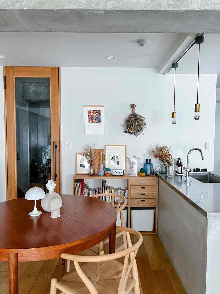 A Nordic style kitchen and living area with white walls and wood tone furniture, featuring a round dining table and pendant lights creating a cozy atmosphere