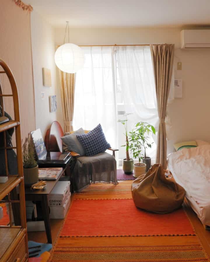 温かみのあるナチュラルなワンルーム寝室、赤いラグとビーズクッション、植物が調和した印象的な空間