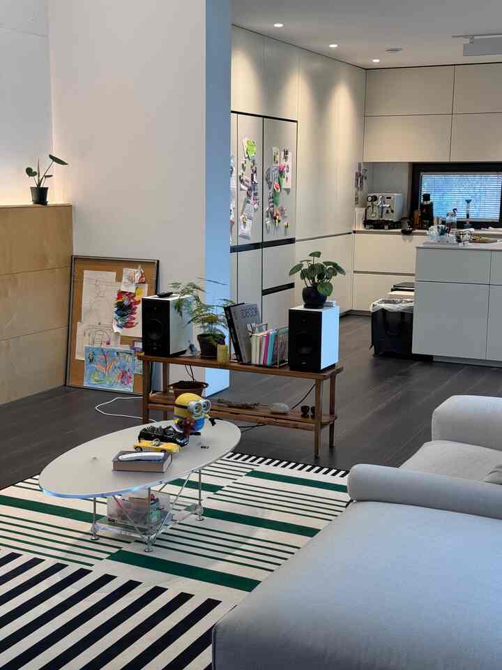 白と緑のトーンのリビング、ミッドセンチュリーモダンのラグとソファ、キッチンアイランドが調和したモダンなインテリア