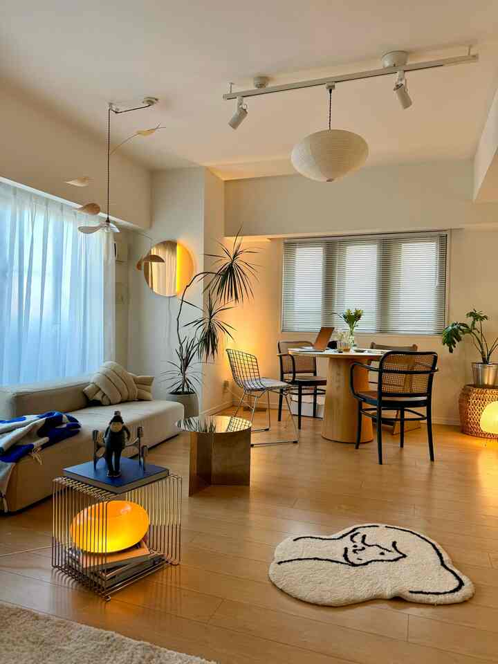 A natural modern dining and living room in beige and wood tones featuring a round dining table and pendant light as focal points