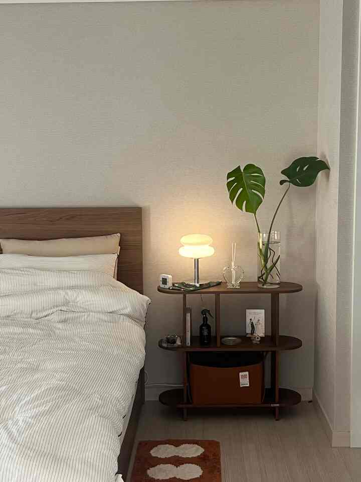 ナチュラルなブラウン調の寝室、木製ベッドとナイトテーブル、大きな植物が配された雰囲気のあるインテリア