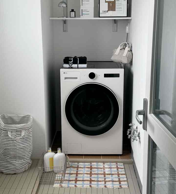 白と茶色の落ち着いた色調のコンパクトなランドリールーム、洗濯機と壁の棚、ランドリーバスケットが配置された実用的な空間
