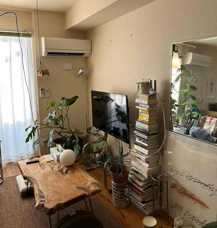 ナチュラルな木目調のリビング、中央に無垢材のコーヒーテーブルと壁掛けテレビ、多数の植物が配置された雰囲気のある空間