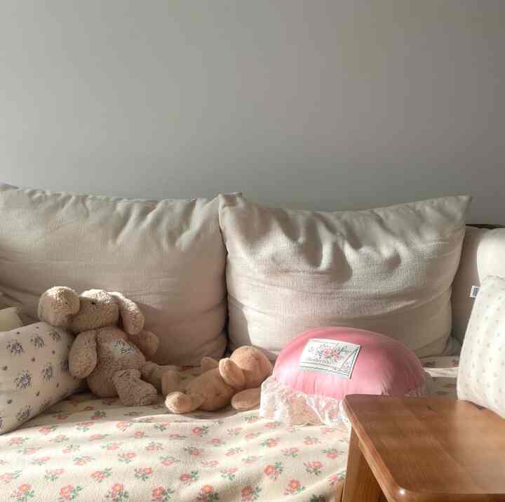 柔らかな白いソファと木目のテーブルが配置された子供部屋、花柄のブランケットとぬいぐるみが暖かい雰囲気を演出