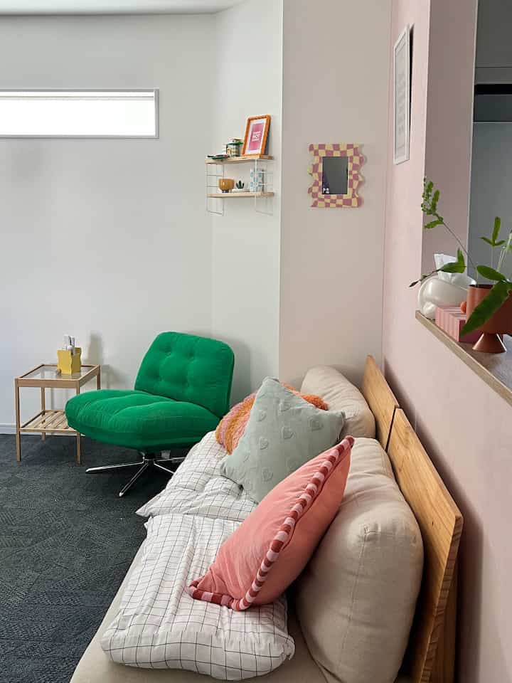 ピンクと緑の色調が印象的なリビング、ベージュのソファと緑のラウンジチェアが配置された雰囲気のある空間