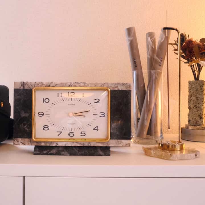ナチュラルカラーの棚にゴールド縁の石製時計とゴールドのお香立てが配置された雰囲気あるインテリアアクセサリー空間
