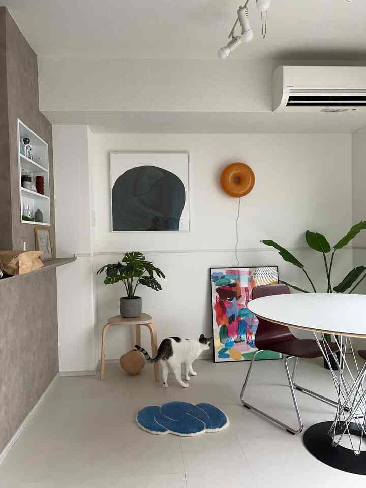 White and modern toned living room featuring a round dining table and a cat, showcasing a clean and minimal interior