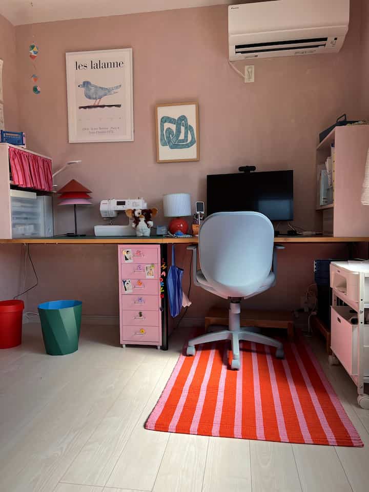 Compact home office with pink and red tones on walls and rug, featuring a modern clean desk and office chair setup