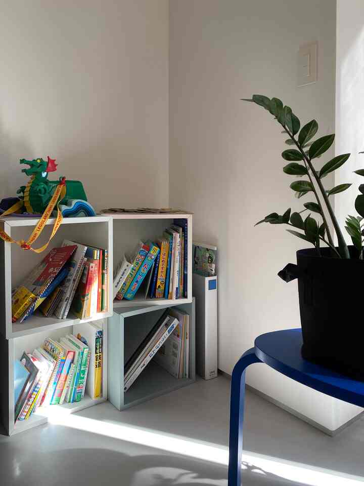 明るい白色の壁と床のダイニングの一角、角度を変えた白いEKET棚に子供の絵本とおもちゃが置かれた雰囲気のあるインテリア