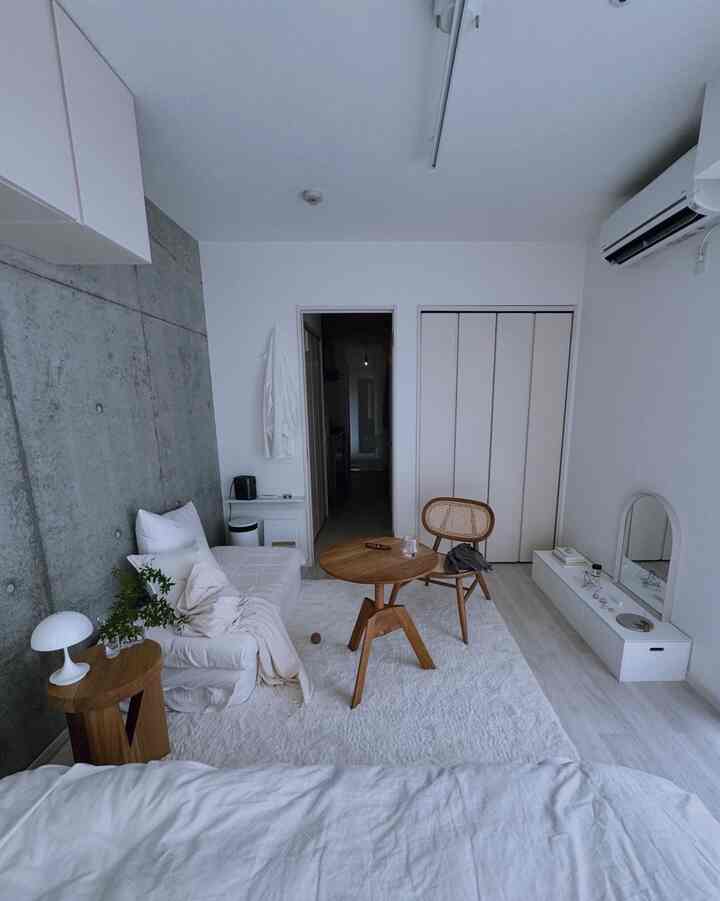 Small living and bedroom space with white and natural wood tones, featuring minimalist furniture and bright atmosphere