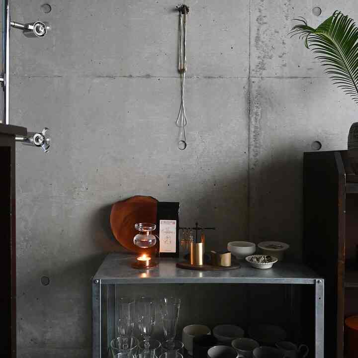 グレーのコンクリート壁を背景に、金属製の棚の上にアロマオイルウォーマーと木製の小物が置かれたナチュラルな雰囲気の静かな空間