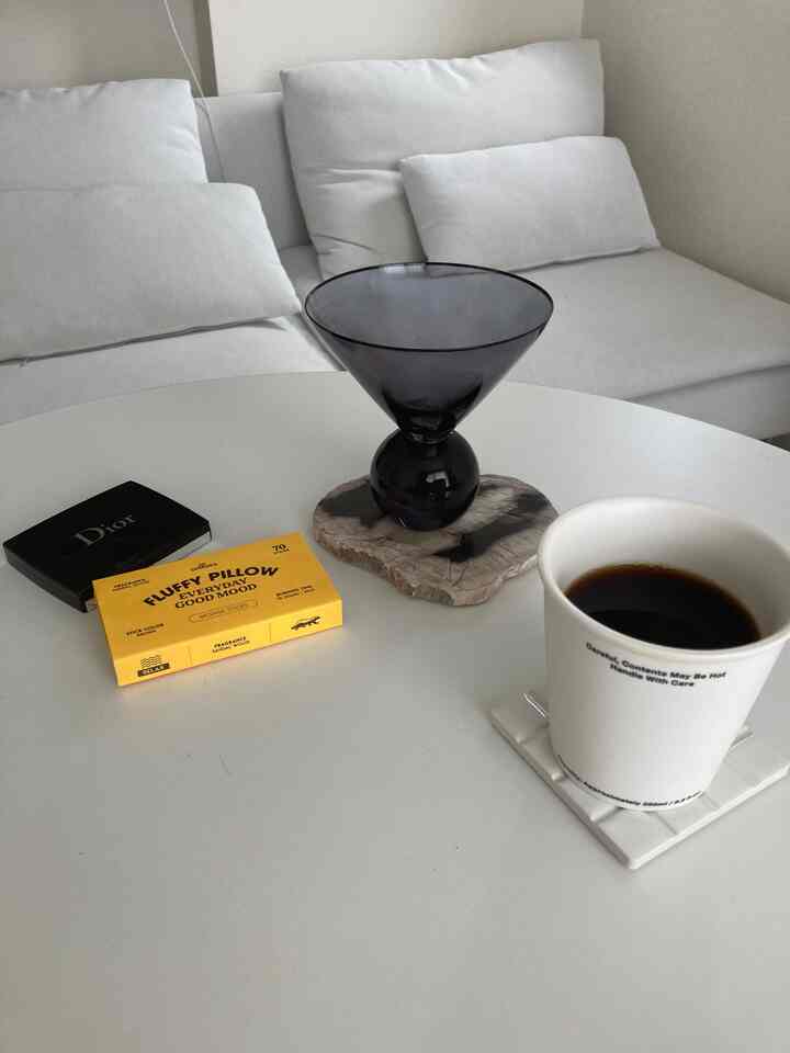 白とモノトーンでまとめられたリビング、白いソファと円形のコーヒーテーブルの上にディフューザーとコーヒーが置かれたシンプルな空間