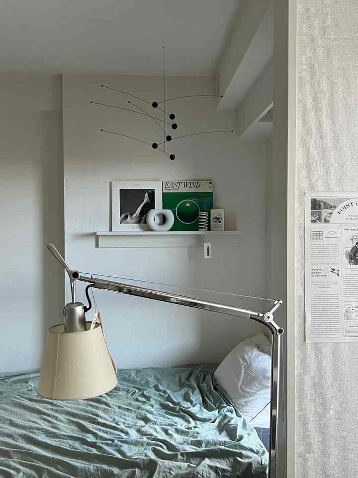 White-walled bedroom with green bedding, natural wood floating shelf and Artemide table lamp creating a modern, calm atmosphere