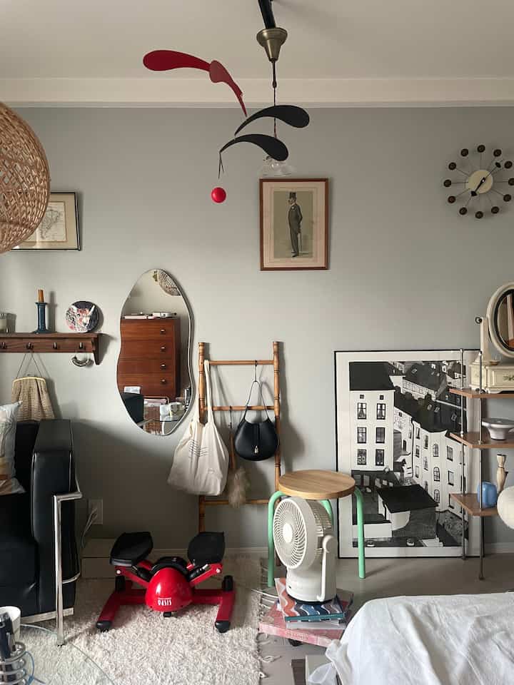 薄いグレーの壁とナチュラルウッドの家具が調和する一人暮らし用1Kリビング、赤いステッパーと小型扇風機が配置された実用的で居心地の良いインテリア