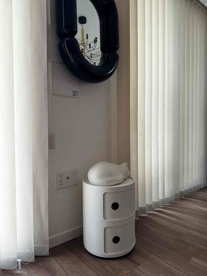 明るい白と木目調の床が調和したコーナースペース、丸い収納の上に猫のオブジェが置かれたシンプルなインテリア