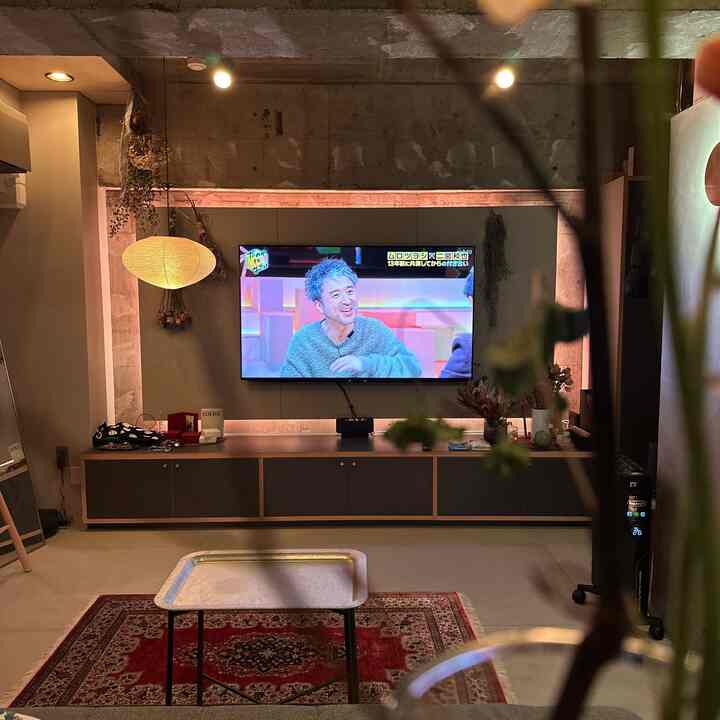 インダストリアルなコンクリート壁と赤いラグのあるリビング、ペンダントライトとテレビ台が配置されたミニマルな空間