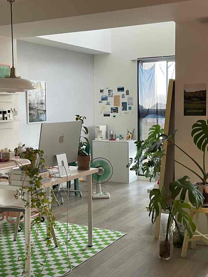 White and green toned studio apartment home office featuring desk, office chair, and various plants with a modern interior