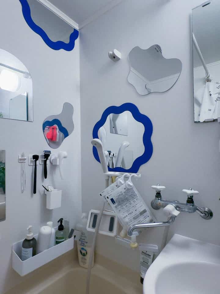 A narrow studio bathroom with white walls featuring blue wavy-shaped mirrors and compact bathroom fixtures