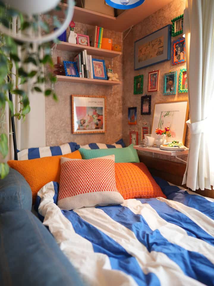 青とオレンジの色調の寝室、クッションと額縁が配置された雰囲気のあるインテリア
