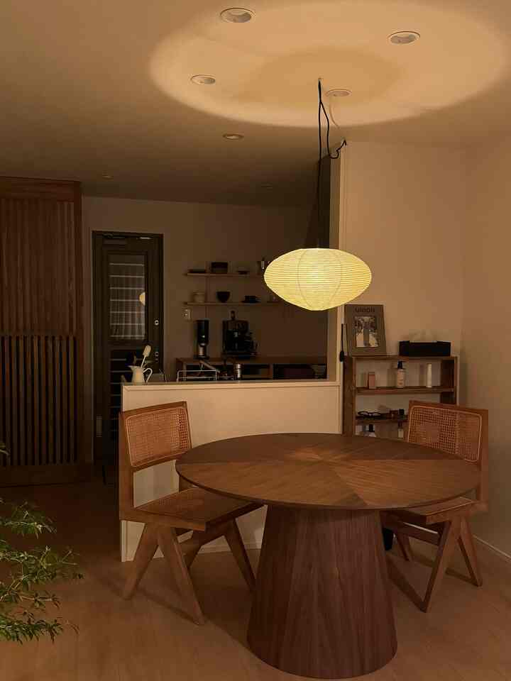 Warm wood tone dining room with round table and chairs, featuring AKARI pendant light creating a cozy modern atmosphere
