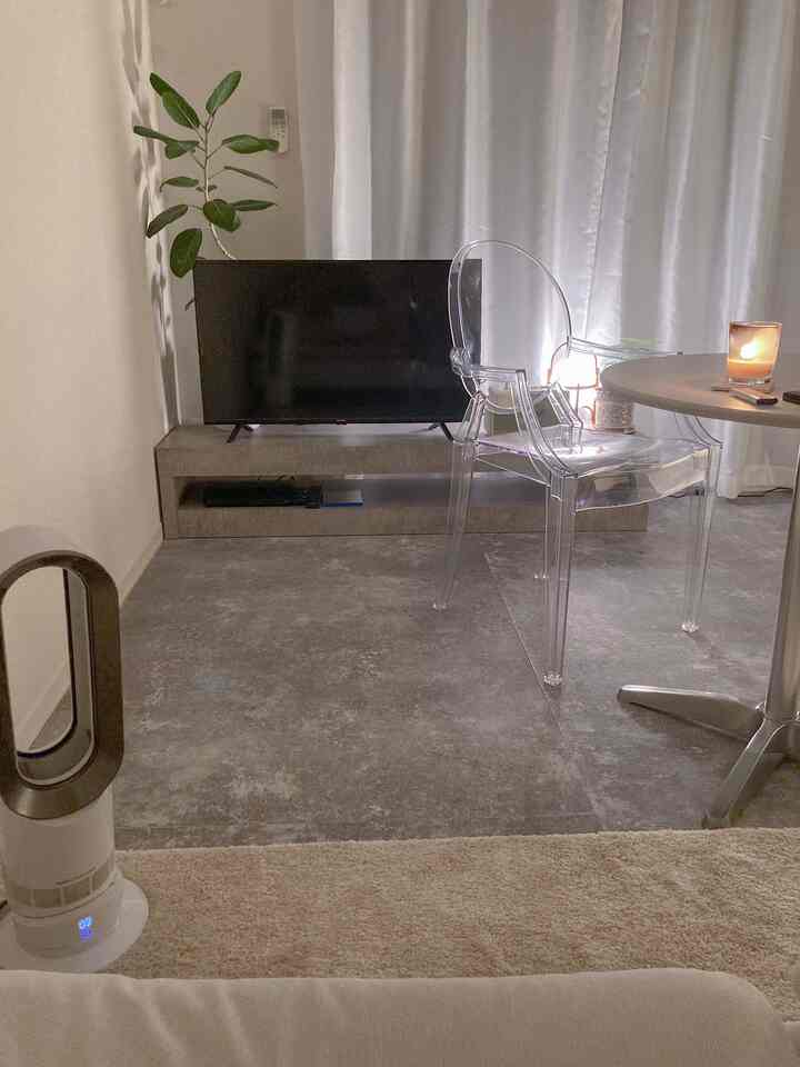 グレーとホワイトのモノトーンの一人暮らし用リビング、透明なアームチェアやテレビ台、キャンドルと植物が配置されたシンプルなインテリア