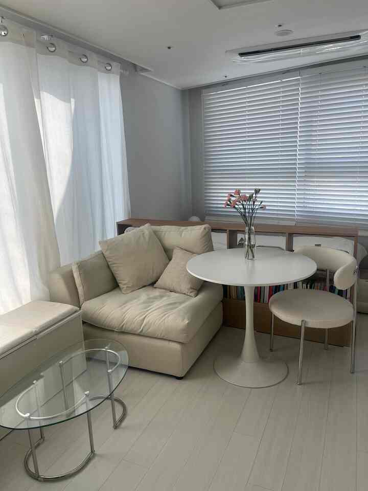 白とベージュのトーンのワンルームリビング、ソファと丸テーブル、本棚が空間を仕切る自然な雰囲気のインテリア