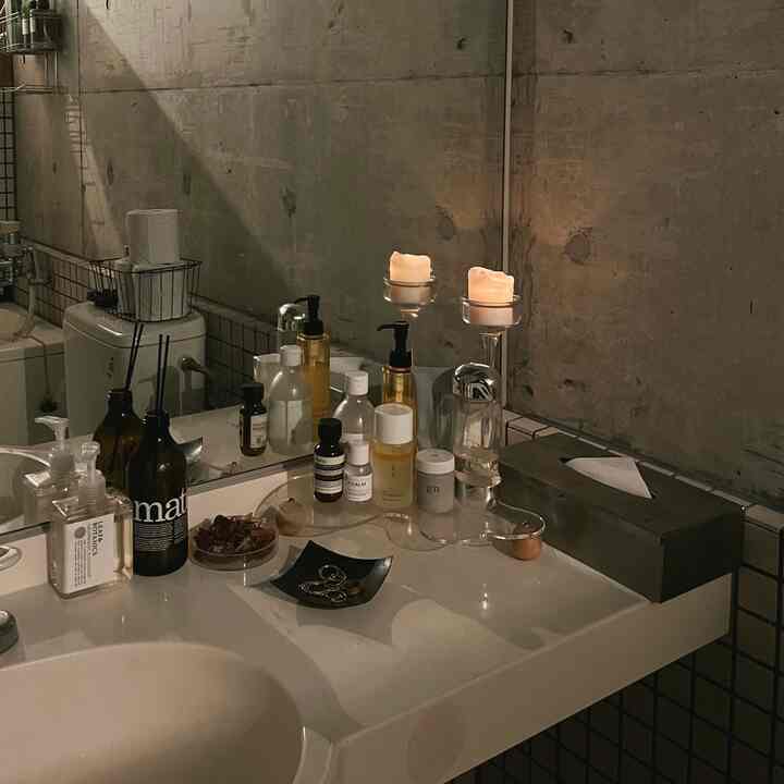 Natural concrete wall bathroom with a white sink and countertop, featuring skincare products and candles arranged neatly
