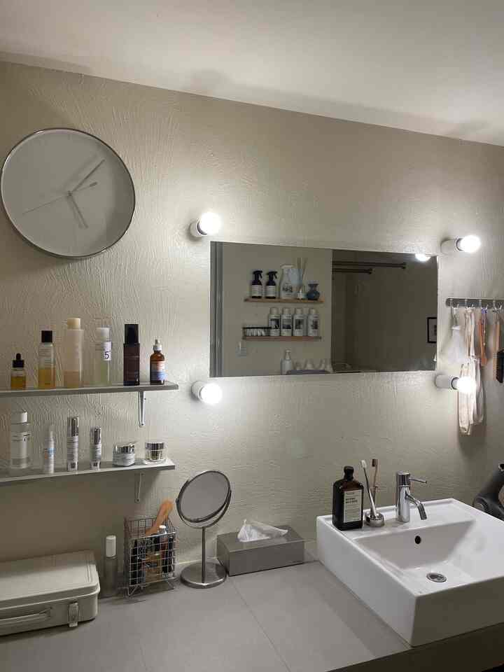 ベージュ色の壁と白い洗面台があるシンプルな1LDKの浴室、鏡と無印良品の工具箱が配置された自然な雰囲気のインテリア