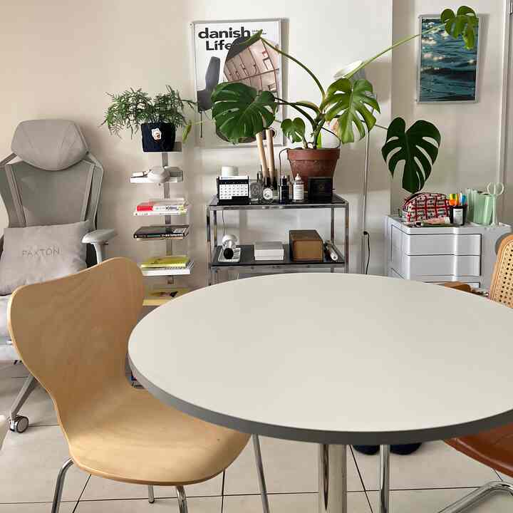 ホワイトとナチュラルトーンが調和したダイニング、丸テーブルと実用的な椅子、ポスターや植物が配置されたシンプルでモダンなインテリア