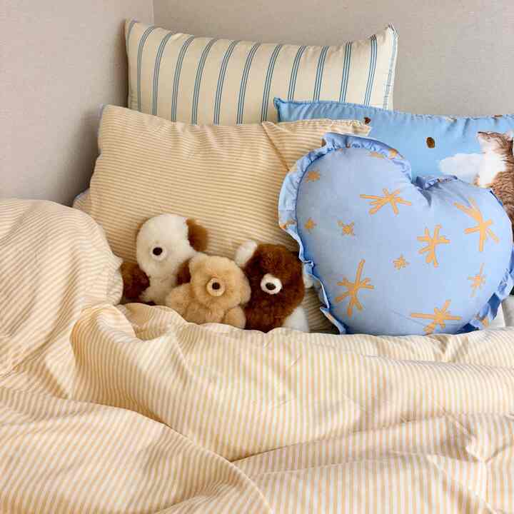 Soft yellow striped bedding in bedroom space featuring blue heart-shaped and cat-print cushions creating a cozy atmosphere