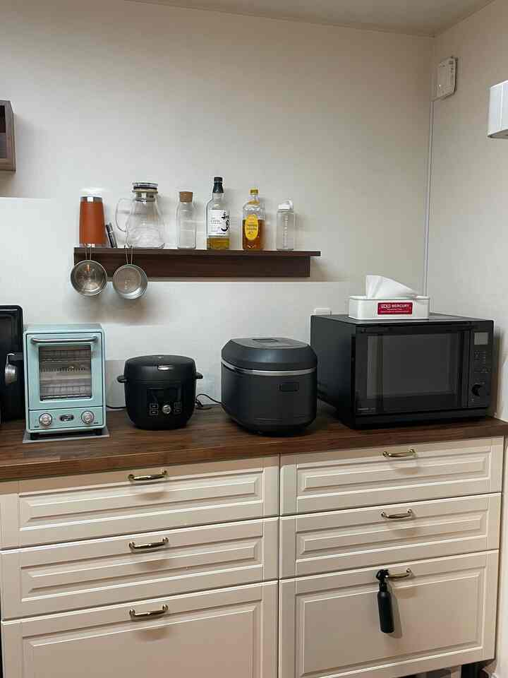 Clean kitchen space featuring white cabinets, natural wood tone shelf, and various kitchen appliances arranged on countertop