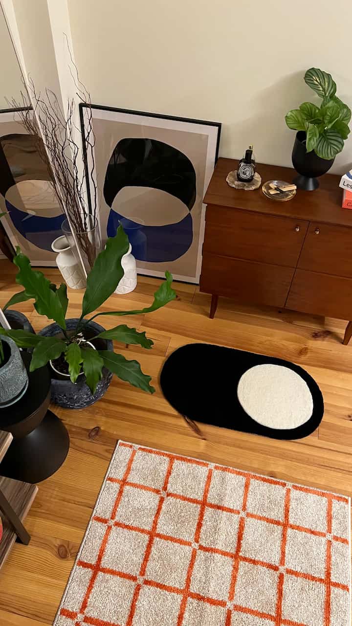 ナチュラルな木目調のリビングルーム、植物やポスター、キャビネットが配置され、落ち着いた雰囲気の空間