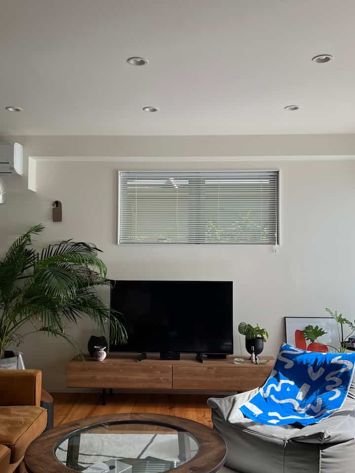 A Nordic living room featuring wood tone and white color scheme, with TV stand, plants, sofa, and coffee table arranged for a cozy atmosphere