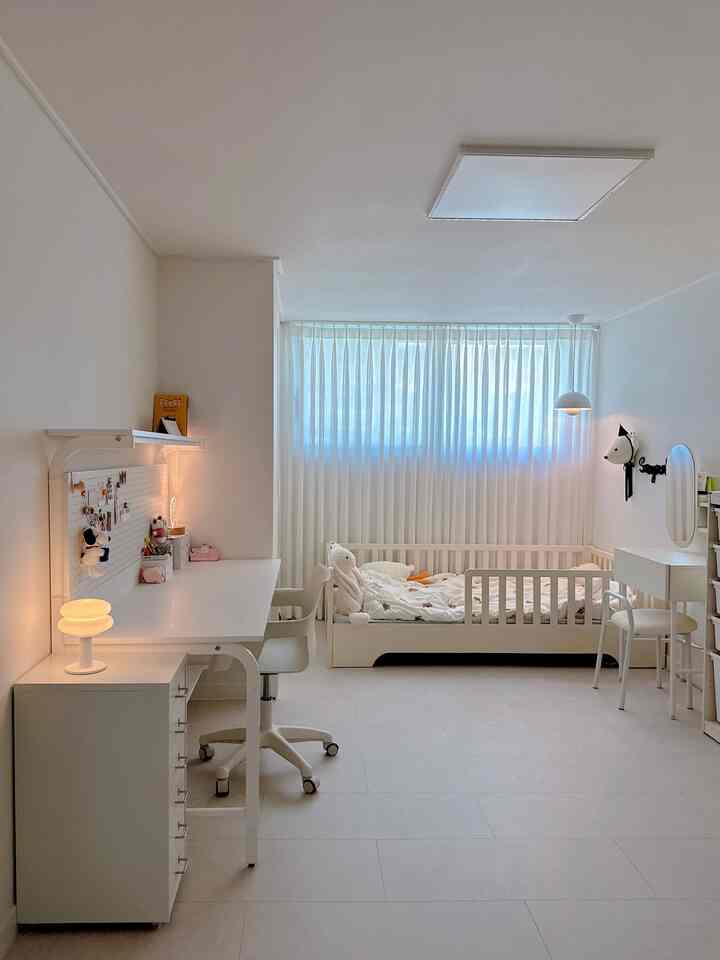 明るいホワイトトーンの子供部屋、低めのベビーベッドとシンプルなデスクが配置された居心地の良い空間