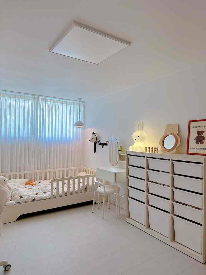 明るいモノトーンの子供部屋、子供用ベッドと化粧台、大型収納が配置された清潔で居心地の良い空間