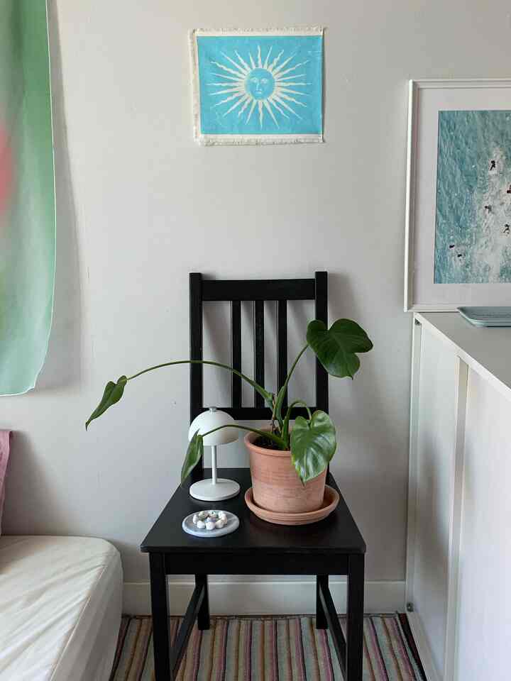 白い壁と黒い椅子が中心のナチュラルトーンの狭い部屋、植物と額縁アートがアクセントのシンプルな空間