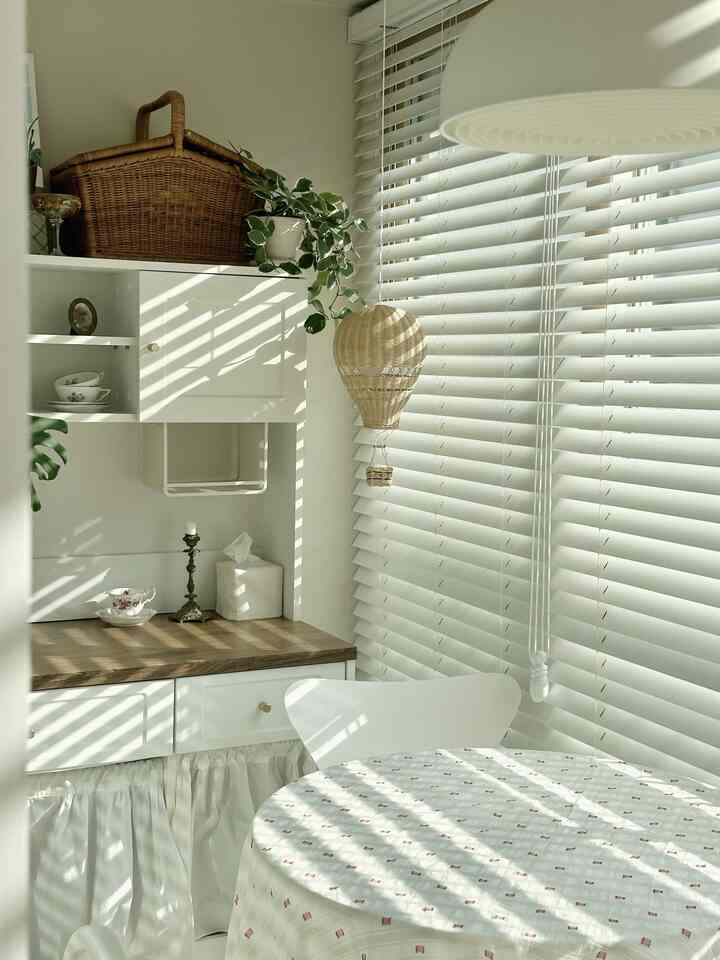 White and natural-toned veranda home cafe featuring a round dining table, rattan basket, and plants creating a cozy atmosphere