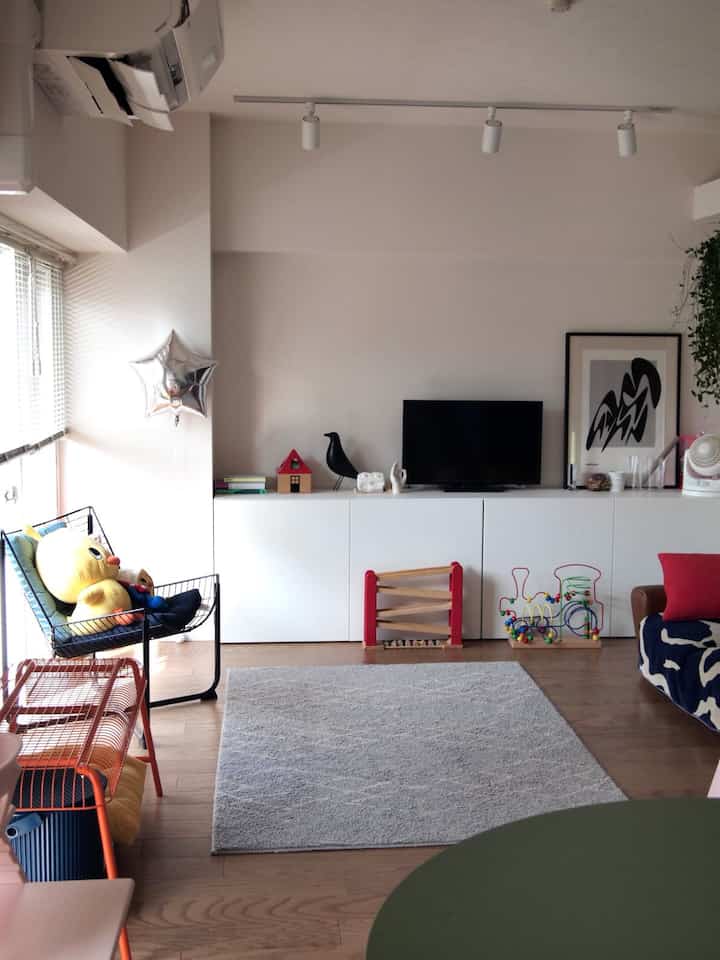 Bright natural-toned living room featuring white BESTÅ storage unit centered against the wall, with children's toys and brown sofa creating a tidy space