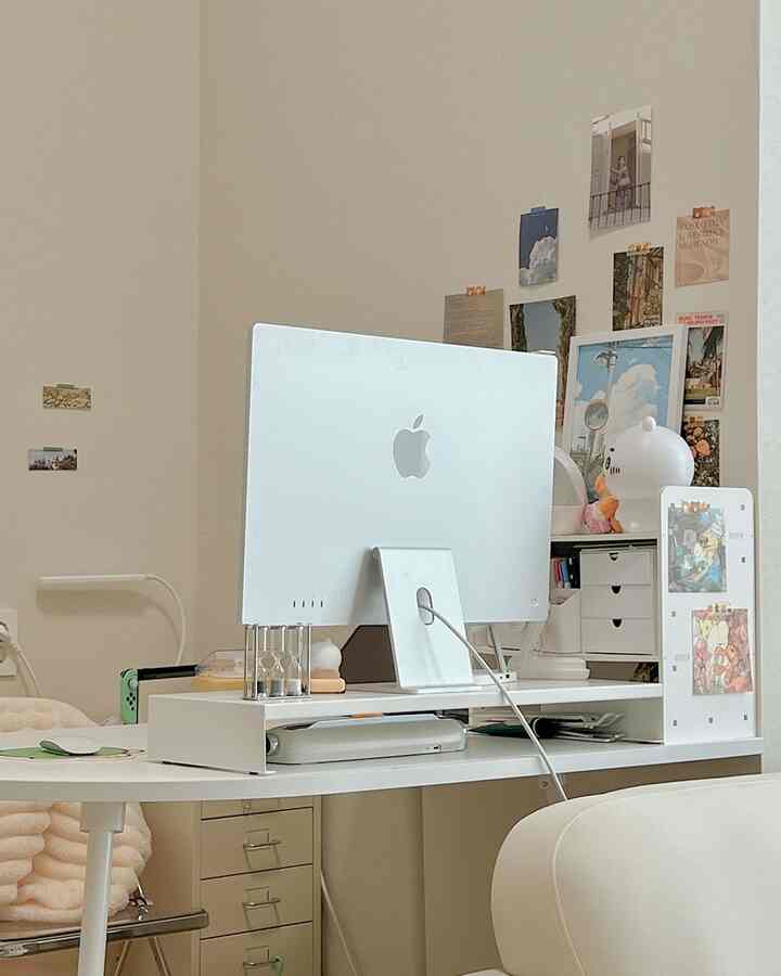 White-toned home office featuring an Apple iMac, white desk, storage drawers, and posters for a neat workspace
