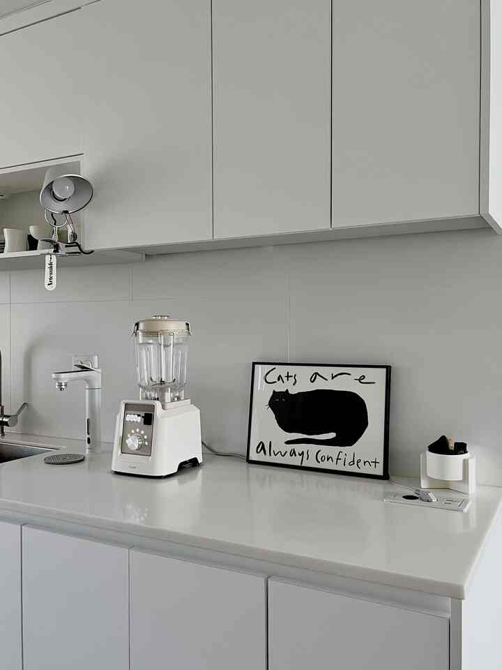 白を基調としたモダンなキッチン、白いブレンダーと黒猫のポスターが配置された清潔感のある空間