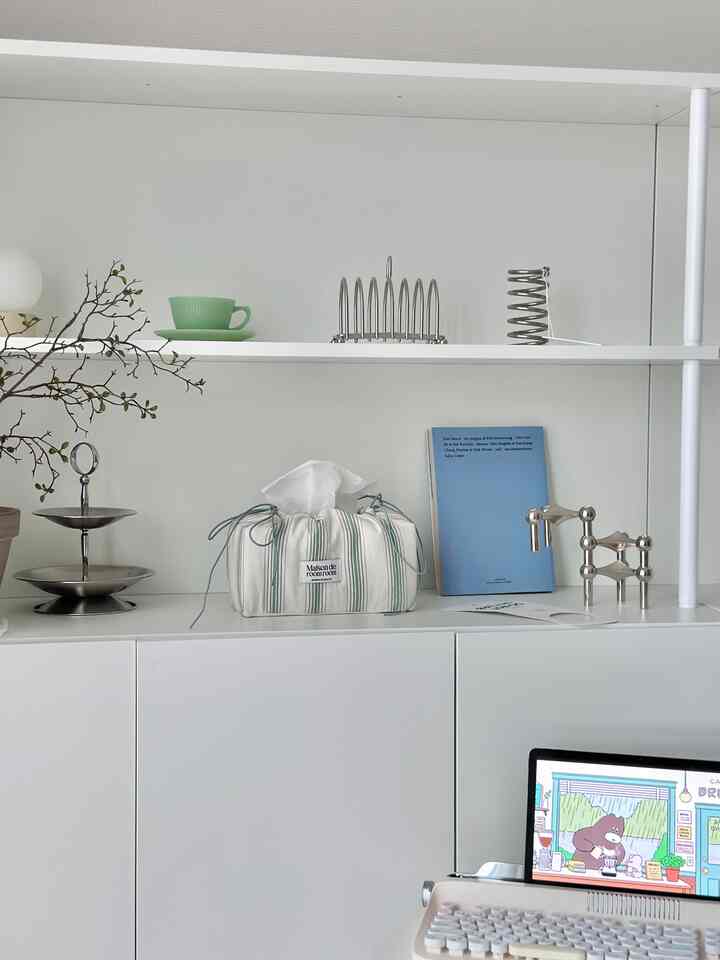 Bright white shelves and storage cabinets feature a clean, simple interior with green plants and a mint cup as accents