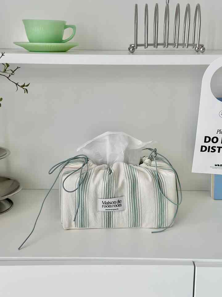 白とベージュのトーンのシンプルな棚の上に収納アイデアが際立つ布製のティッシュケースとグリーンのカップが配置された落ち着いた空間